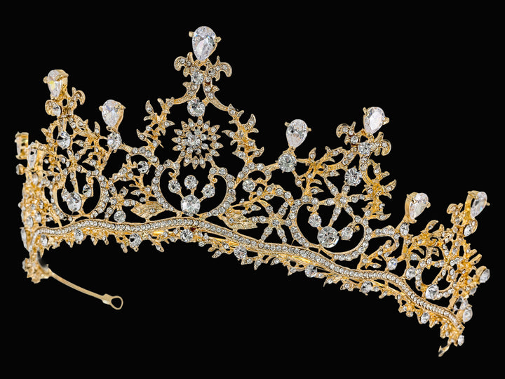 Side-angle shot of a gold-plated tiara with pear-shaped cubic zirconia, round clear stones, and intricate filigree scrollwork.